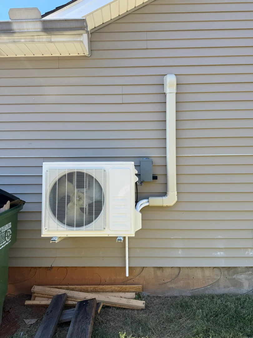 A ductless mini split condenser with its insulated line set running up the vinyl siding to the indoor head